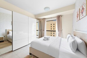 Moderni hotellihuone, jossa on suuri sänky, vaatekaappi ja ikkunasta avautuva näkymä toiseen rakennukseen.