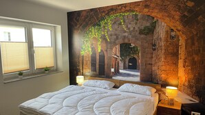 Een slaapkamer met een groot bed, een raam met zonwering, een muurschildering van een boog en een nachtkastje met een lamp.