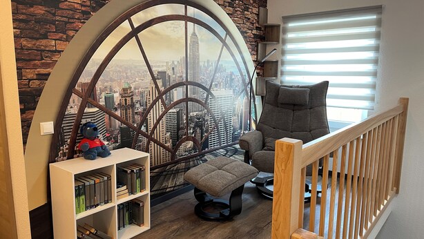 Een gezellige leeshoek met een groot raam, een comfortabele fauteuil, een klein boekenrek en een decoratieve boog.