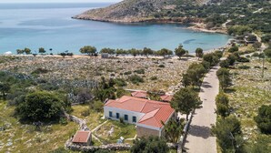 Une propriété située sur la côte, avec un chemin pavé menant à un bâtiment doté d’un toit rouge, entouré d’arbres et d’un terrain rocheux.