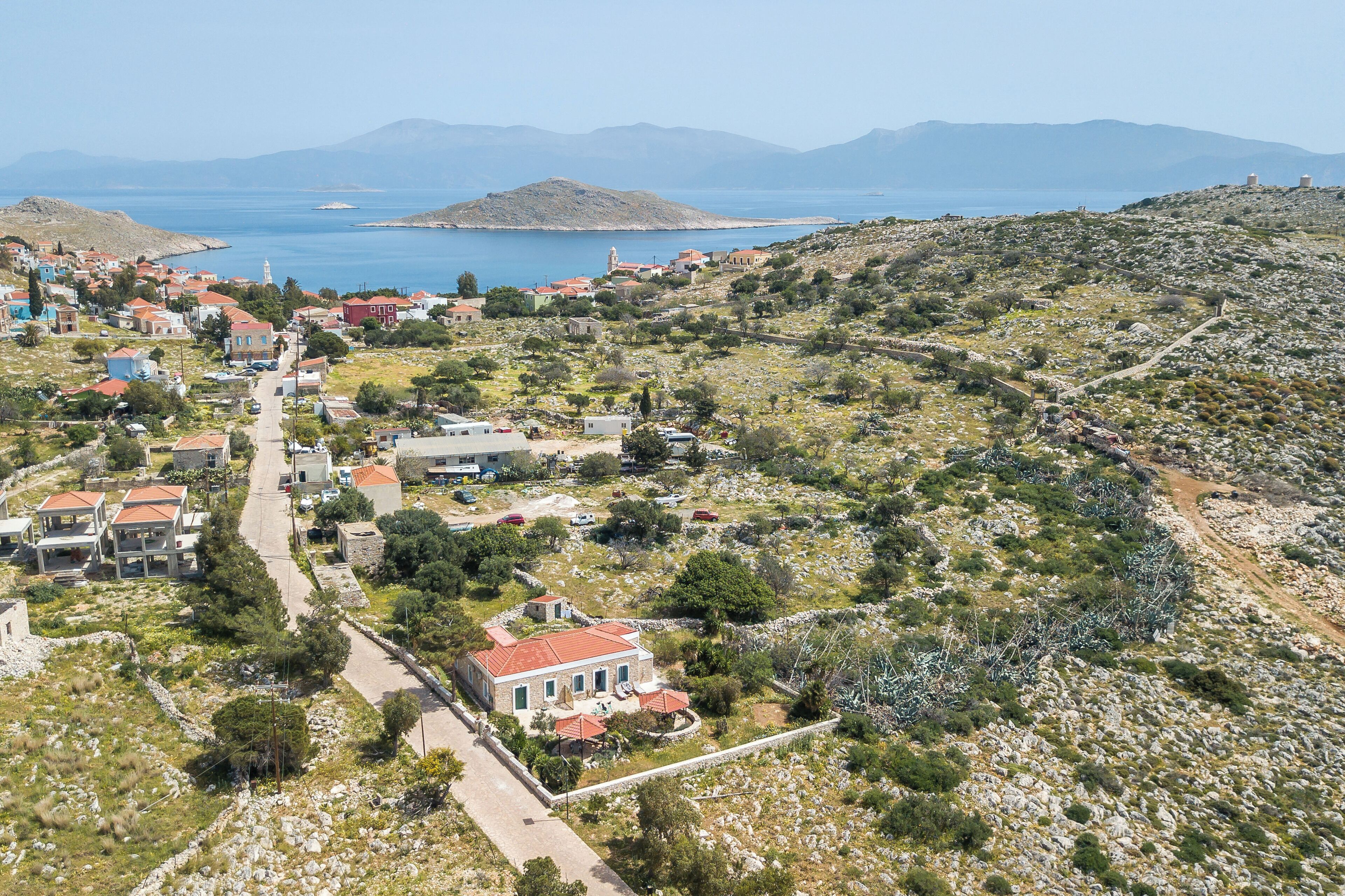 A coastal village with stone houses, a central road, and a view of the sea and mountains.