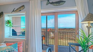 A room with a view of the beach, a blue chair, a table with a checkered tablecloth, and a lamp. - 2 Pools + Pickleball + Boardwalk | Steps to Sand | Seaside Escape (Port Aransas)