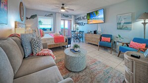 A living room with a sofa, armchair, coffee table, and a TV on the wall. - 2 Pools + Pickleball + Boardwalk | Steps to Sand | Seaside Escape (Port Aransas)