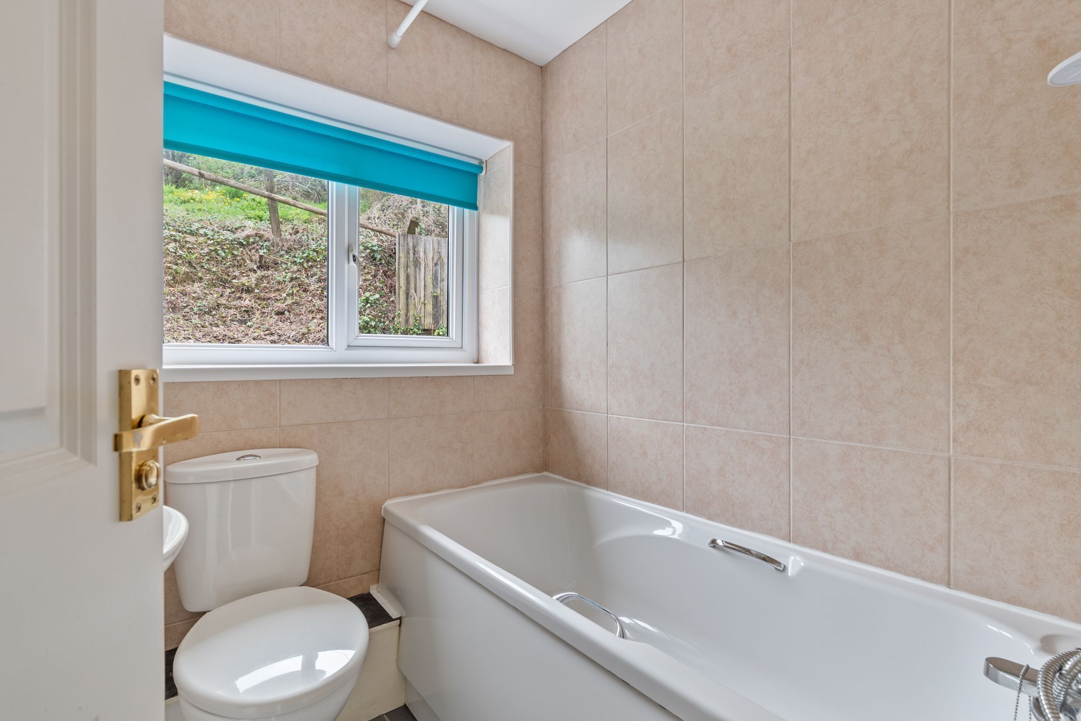 Une salle de bain avec une baignoire blanche, des toilettes et une fenêtre avec un store bleu.