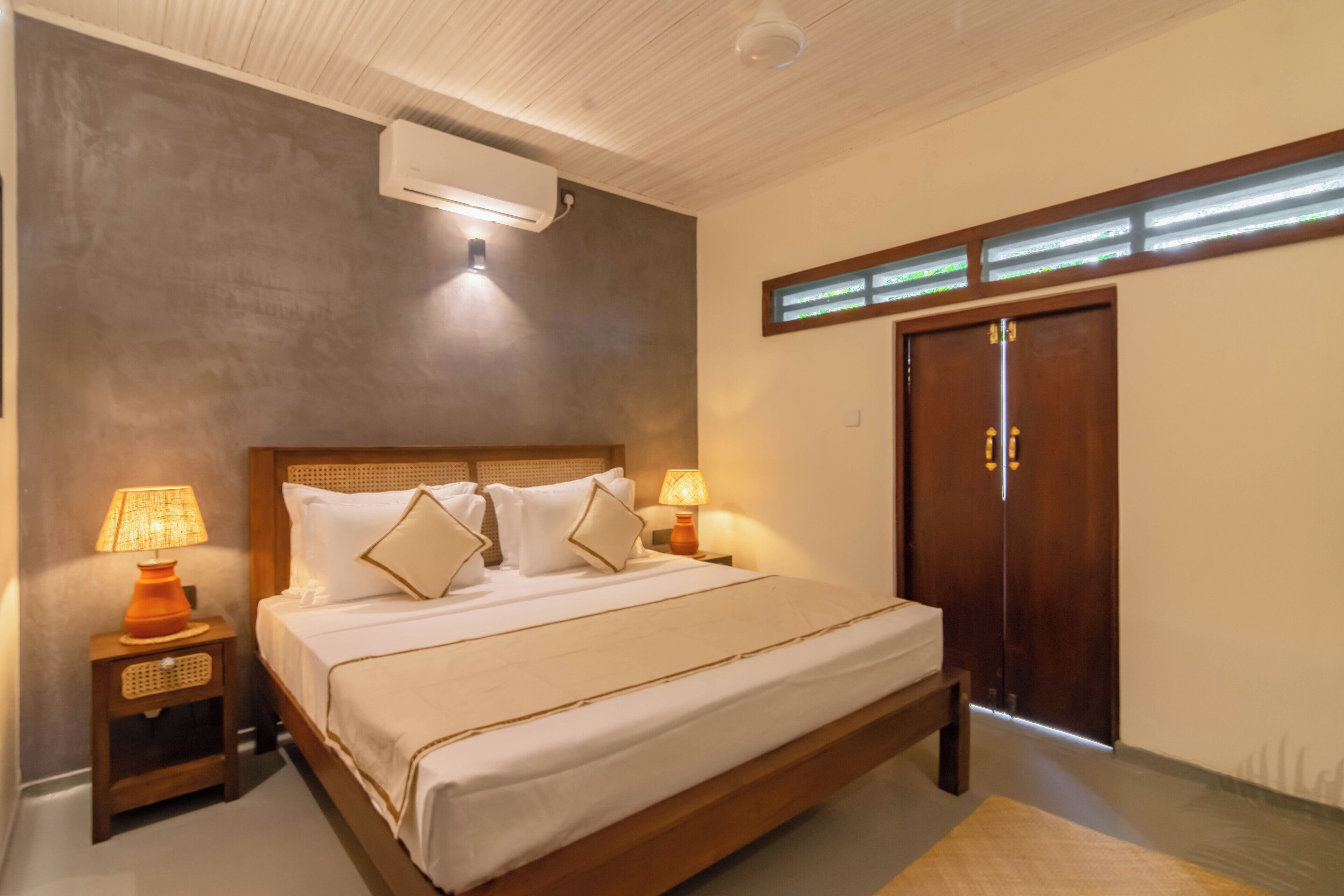 A bedroom with a large bed, two bedside tables with lamps, a wooden headboard, a wardrobe, and a ceiling fan.