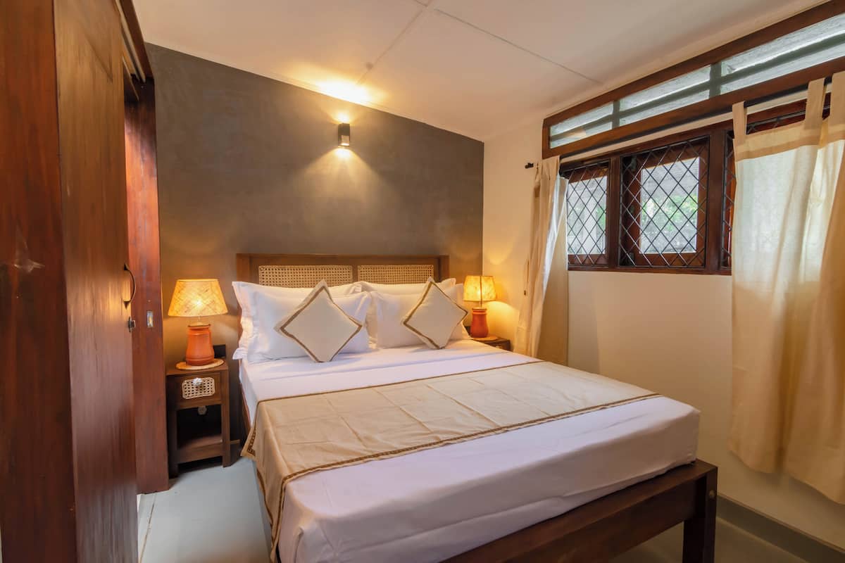 A neatly made bed with a headboard, two bedside lamps, and a window with curtains.