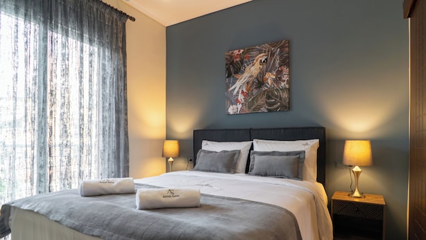 Un letto rifatto con un piumone grigio e bianco, due abat-jour e un quadro a tema tropicale sulla parete.