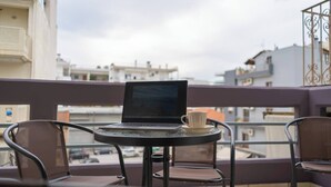 Un balcone con un laptop su un tavolino rotondo, una tazza bianca e due sedie in vimini.