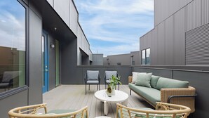 A modern outdoor patio with a round table, wicker chairs, a green sofa, and a blue door.