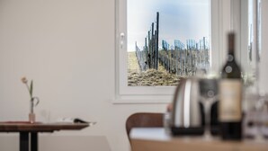 A dining area with a table, chairs, a wine bottle, and a framed picture of a fence and field. - Winzerhäuser Skringer (Leutschach)
