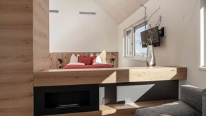 A modern loft bedroom with a wooden slatted ceiling, a built-in bed, a TV mounted on the wall, and a window with a view. - Winzerhäuser Skringer (Leutschach)