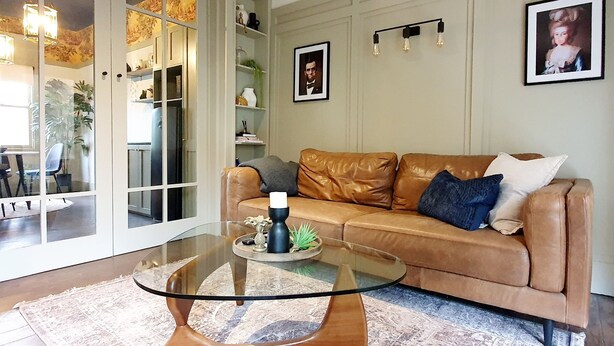 A living room with a glass coffee table, a brown leather sofa, and a patterned rug. - "The Chadwick" Unique, High-end Boutique. (Soldiers Hill)