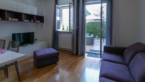 Uma sala de estar moderna com televisão de tela plana, um sofá, uma mesa de jantar e uma porta de vidro deslizante que dá para uma área externa.