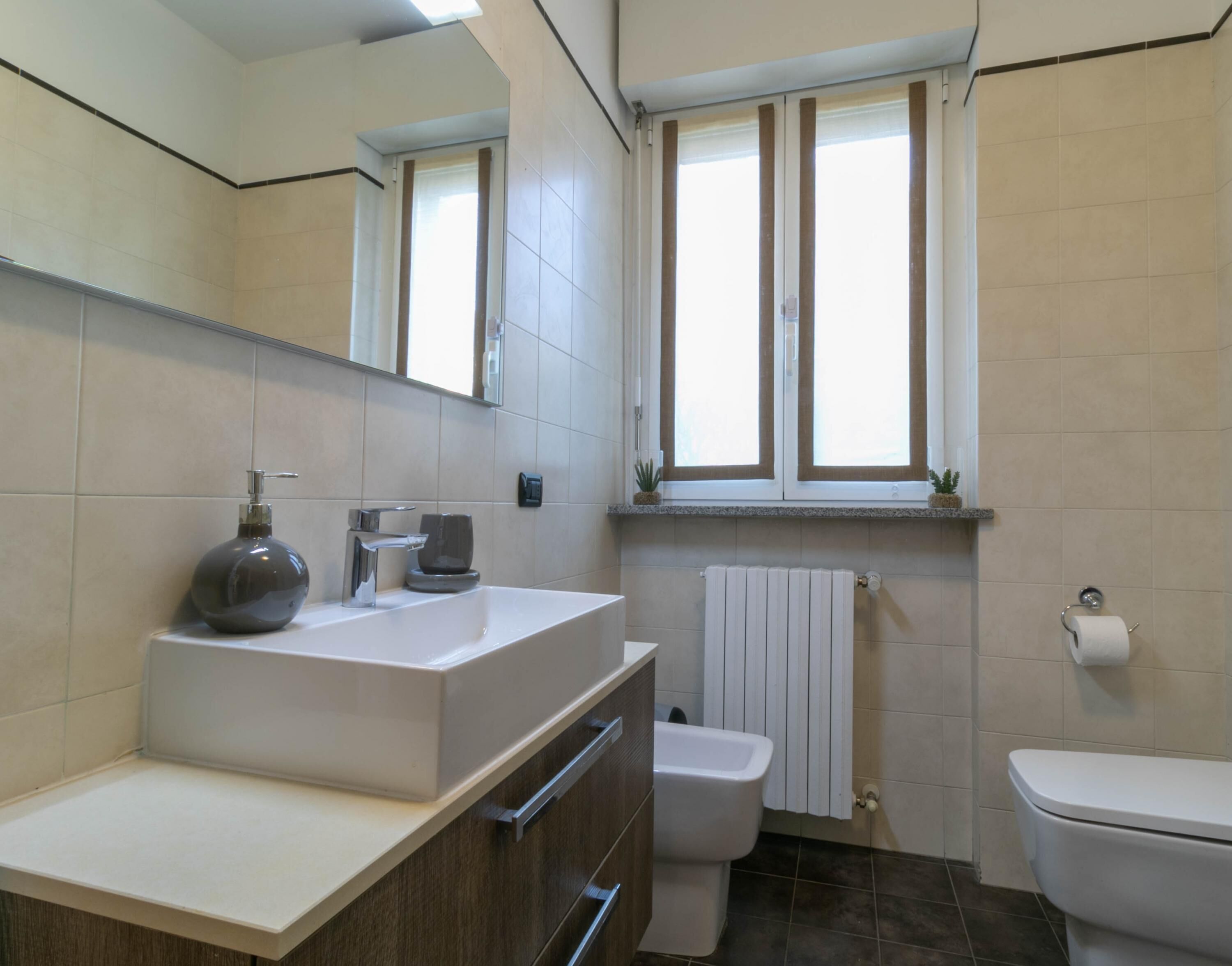 A bathroom with a white sink, a toilet, and a window with a towel hanging on the wall.