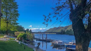 A serene lakeside scene with boats docked, a grassy area, and trees. - Ponte Vecchio Family Apartment (Lecco)