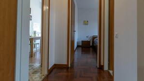 A hallway with wooden flooring and white walls, leading to a bedroom with a bed and a nightstand. - Ponte Vecchio Family Apartment (Lecco)