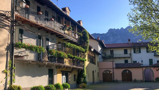 A courtyard with buildings featuring balconies, some with plants, and a mountain in the background. - Ponte Vecchio Family Apartment (Lecco)