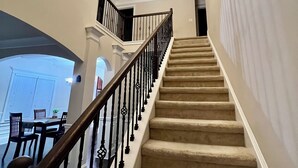 A staircase with a wooden handrail and beige carpet, leading to a landing with a chandelier.