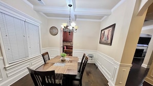 A dining room with a wooden table, black chairs, a chandelier, a clock, and a framed picture on the wall.
