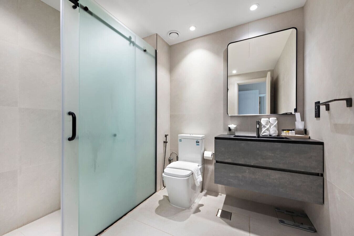 Et moderne badeværelse med brusekabine i glas, toilet og vaskebord med spejl.