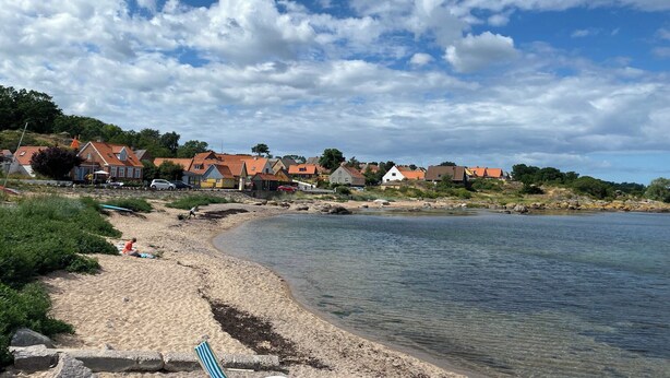 Une plage avec des maisons en arrière-plan, un ciel dégagé et une eau calme.