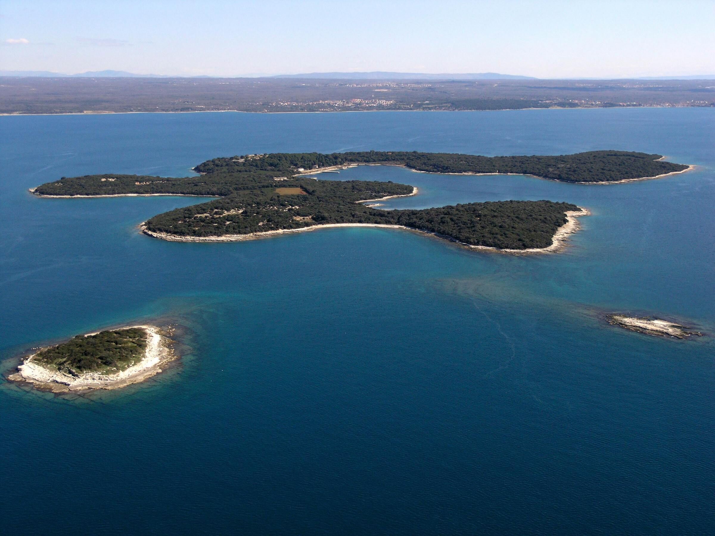 An aerial view of a cluster of islands with clear blue waters and a distant coastline.