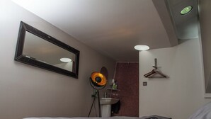 Ein Schlafzimmer mit einem Bett, einem großen Spiegel, einer Nachttischlampe, einer Hängelampe, einem Handtuch und einer Wand mit roten und weißen Fliesen.