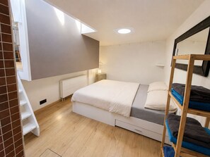 Un dormitorio con literas, un radiador blanco, una mesita de noche con lámpara y una ventana.