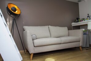 Una habitación con un sofá gris, una lámpara de pie y un escritorio con diversos objetos.