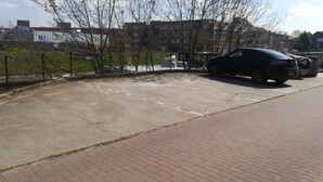 Ein Parkplatz mit befestigtem Belag, ein schwarzes Auto und ein Pflasterweg.