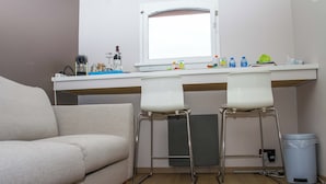 Ein kleiner, moderner Raum mit einer Couch, zwei Barhocker, einem Schreibtisch mit einem Computer und einem Fenster.