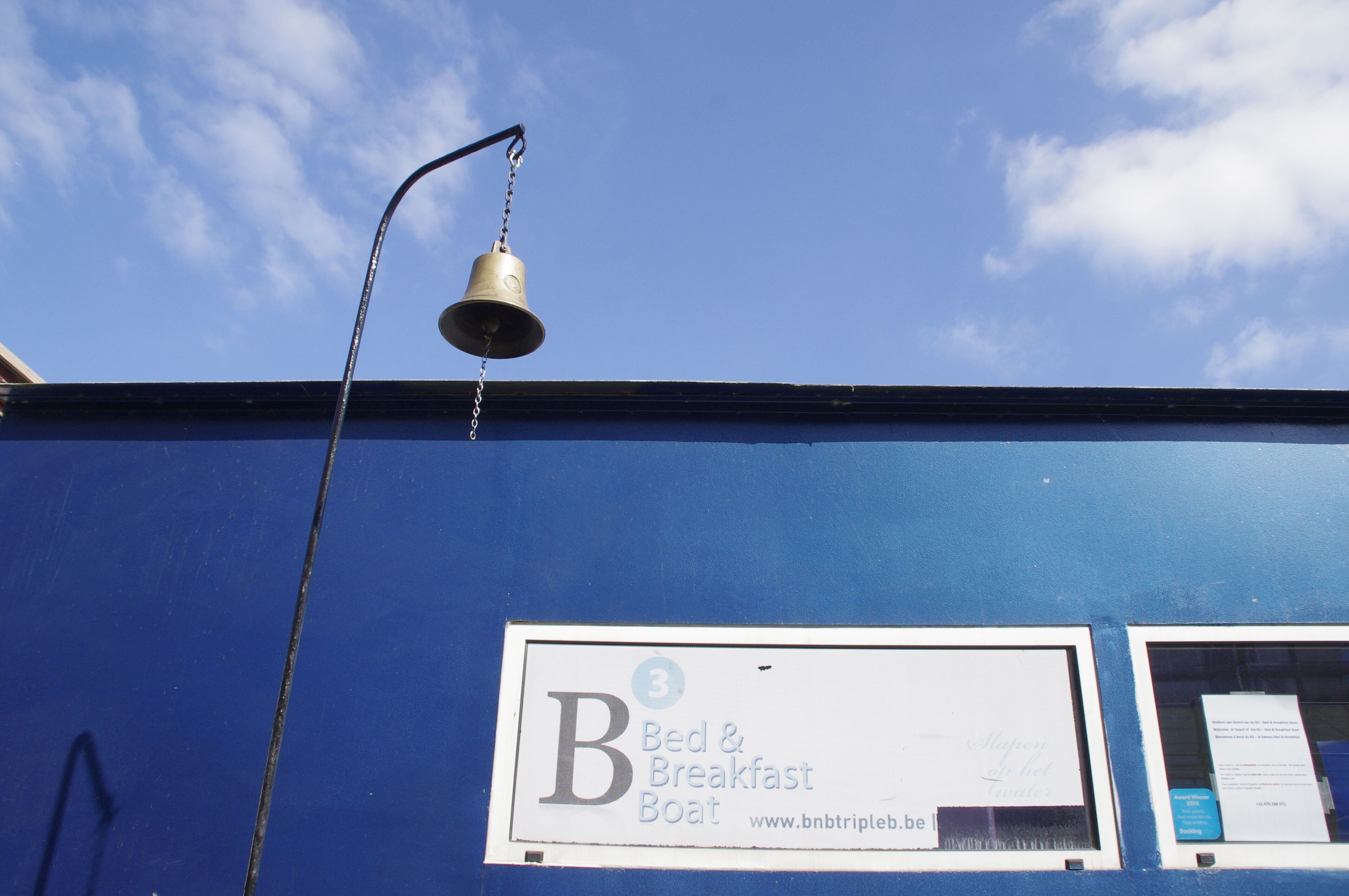 A blue building with a sign for 'Bed & Breakfast Boat' and a bell hanging from a pole.