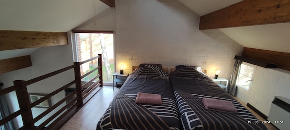 Une chambre avec deux lits, un plafond en bois, un mur en briques et une fenêtre.