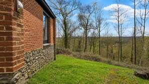 A brick building with a stone foundation, a grassy yard, and a forested area in the background. - Havane13 -Quietly located, fully furnished holiday home (Hastiere)
