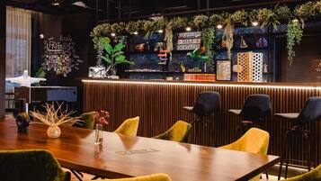 Un espace bar moderne avec un comptoir en bois, des chaises vertes et un mur décoré de plantes et de photos.