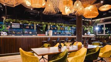 Un restaurant avec un bar en bois, des chaises jaunes et des lampes en osier suspendues au plafond.