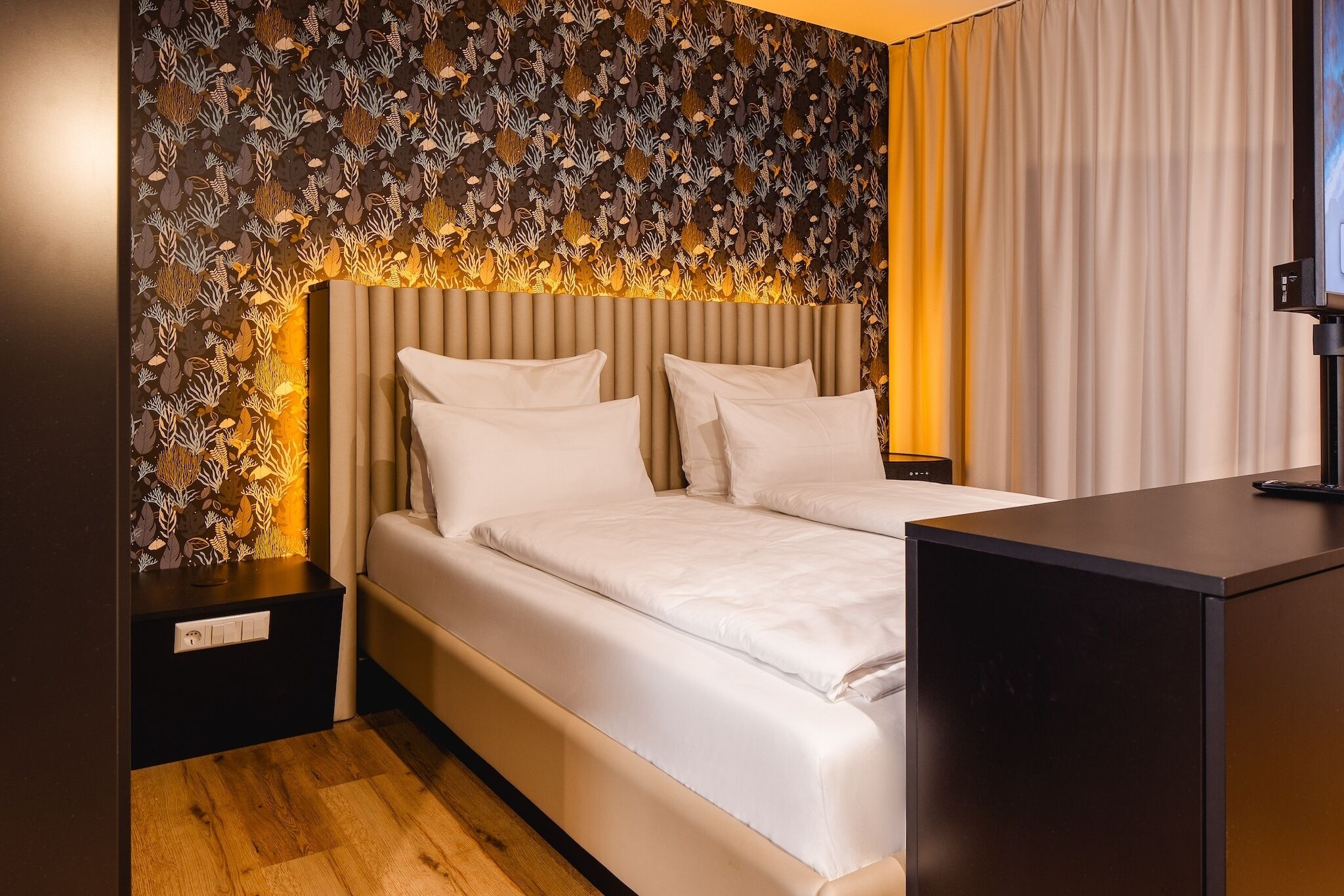Una habitación de hotel moderna con una cama, una mesita de noche, un escritorio y una pared con diseño.