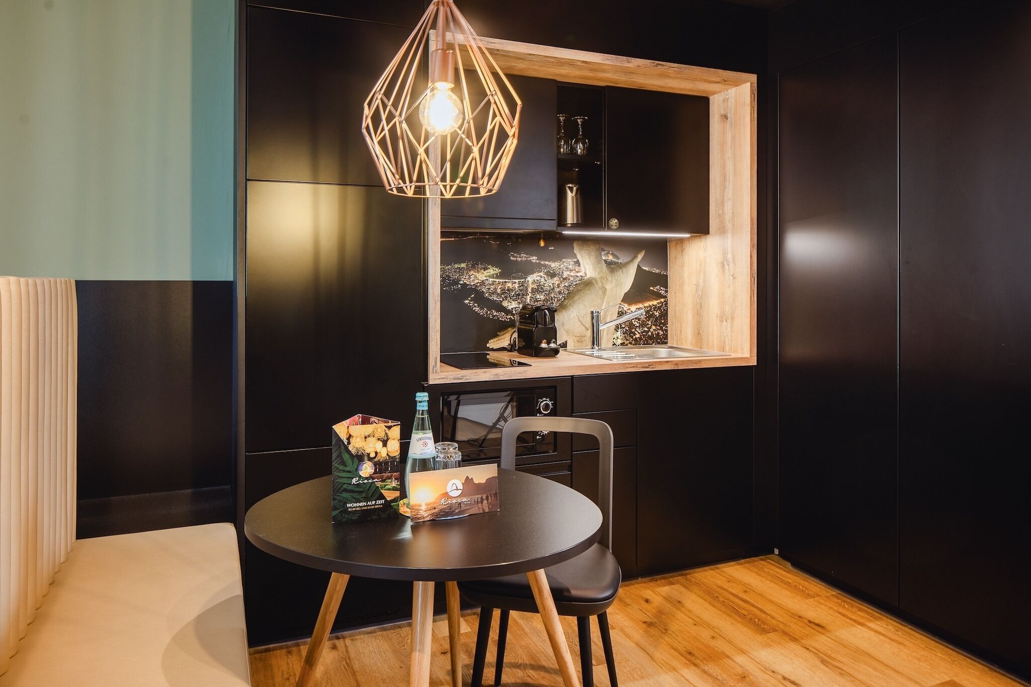 A compact kitchen with a wooden countertop, a hanging light fixture, and a window with a cityscape view.