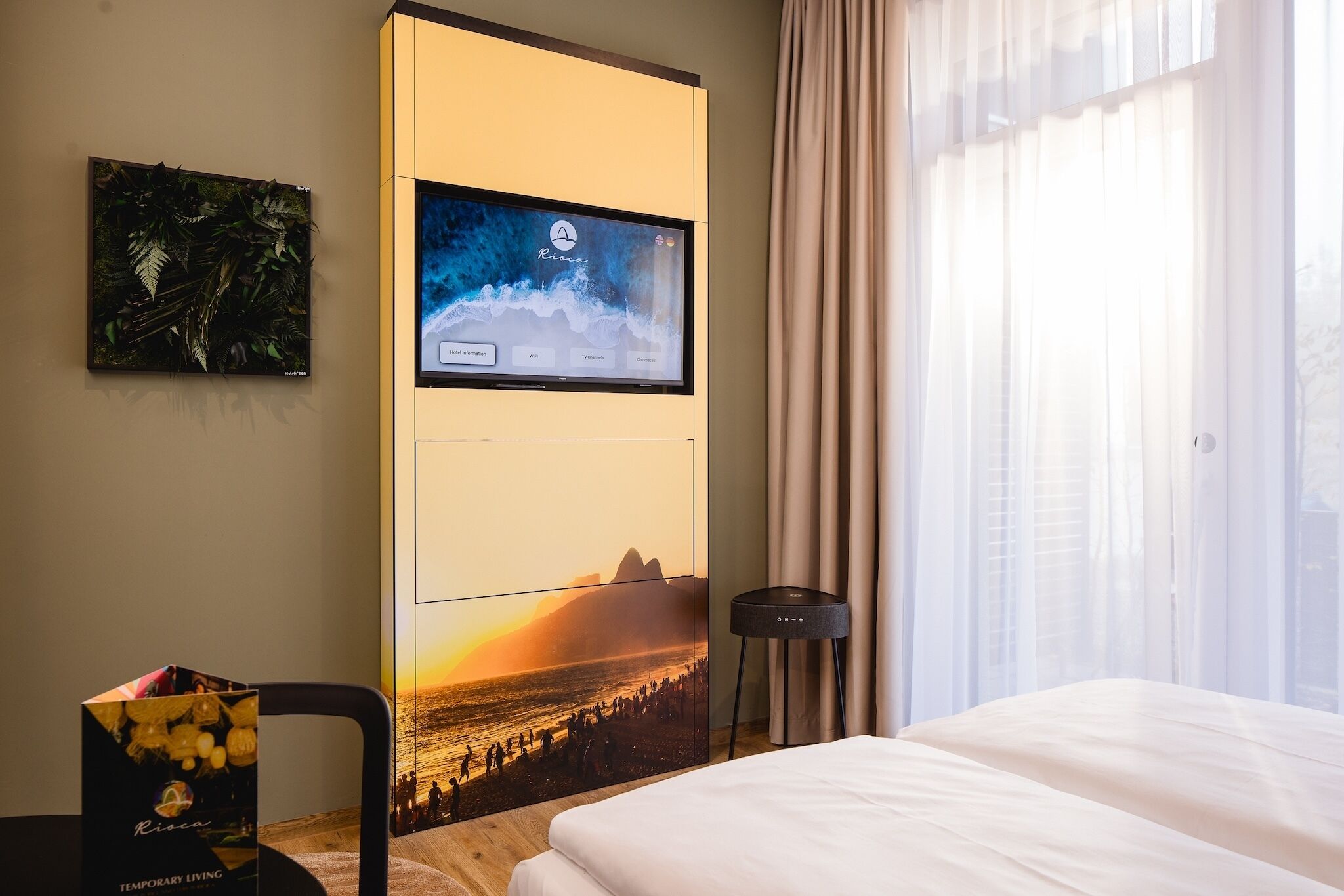 A hotel room with a bed, a flat-screen TV mounted on a wall, a small table, and a window with curtains.