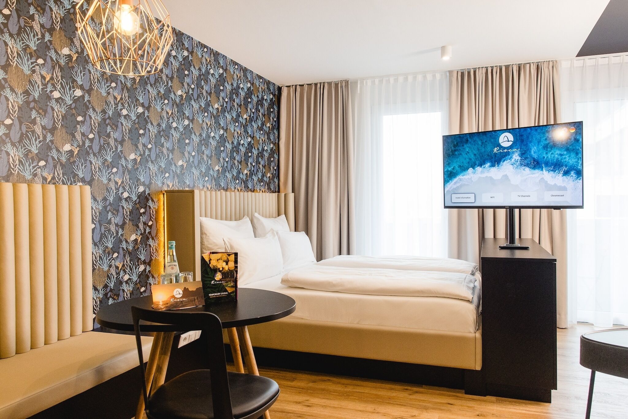 Una habitación de hotel moderna con una cama, un escritorio, un televisor y una pared con un diseño de hojas.