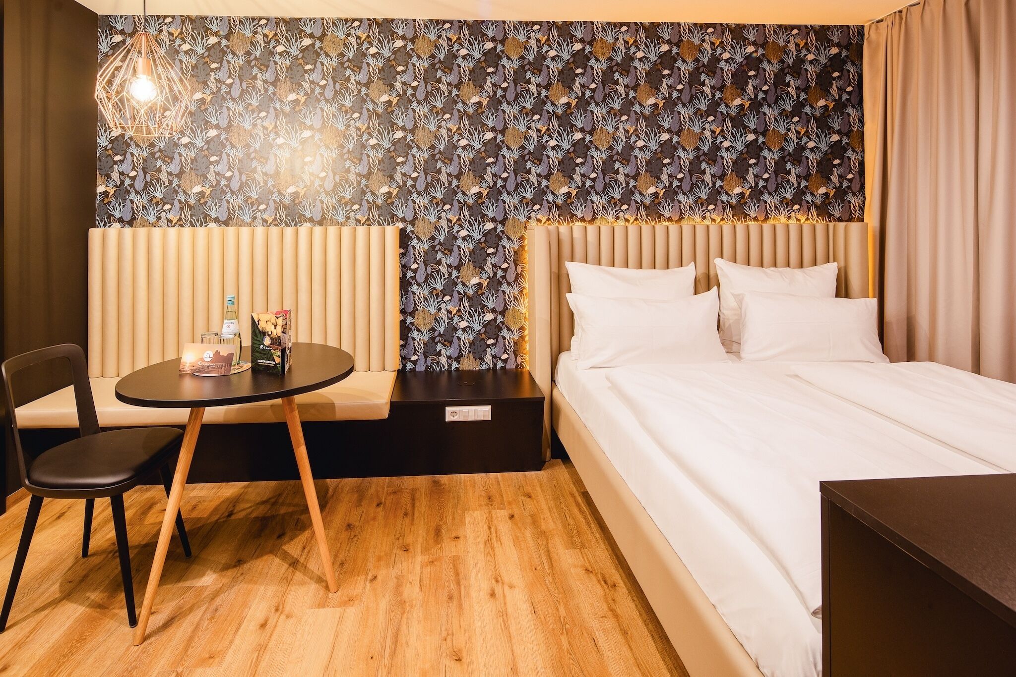 A hotel room with a bed, a round table with a chair, a decorative wall, and a hanging light fixture.