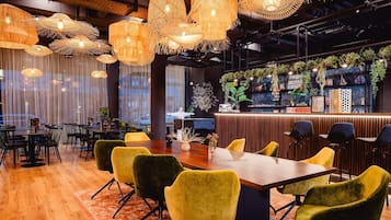 A modern restaurant with a wooden table and yellow chairs, surrounded by hanging wicker lamps.