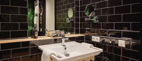 Un baño moderno con paredes de azulejos negros, un lavamanos blanco y un espejo con dos espejos redondos.