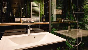 Un baño moderno con un lavabo grande de color blanco, un cabezal de ducha manual y una zona de ducha con mampara de cristal y plantas.