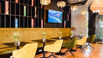 Un restaurant moderne avec des tables noires, des chaises jaunes et vertes, et un téléviseur diffusant des images d’un paysage pittoresque.
