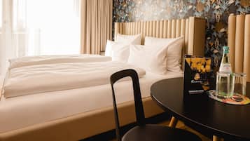 Une chambre d’hôtel avec un lit, une chaise, une table sur laquelle se trouvent une bouteille et un verre, ainsi qu’un objet décoratif.