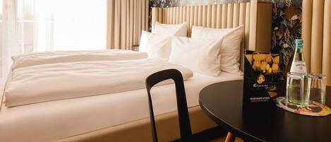 A hotel room with a bed, a chair, a table with a bottle and a glass, and a decorative item on the table.