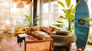 A modern living room with a leather sofa, a wooden chair, a surfboard, and potted plants. - Rioca Konstanz Posto 10 (Konstanz)