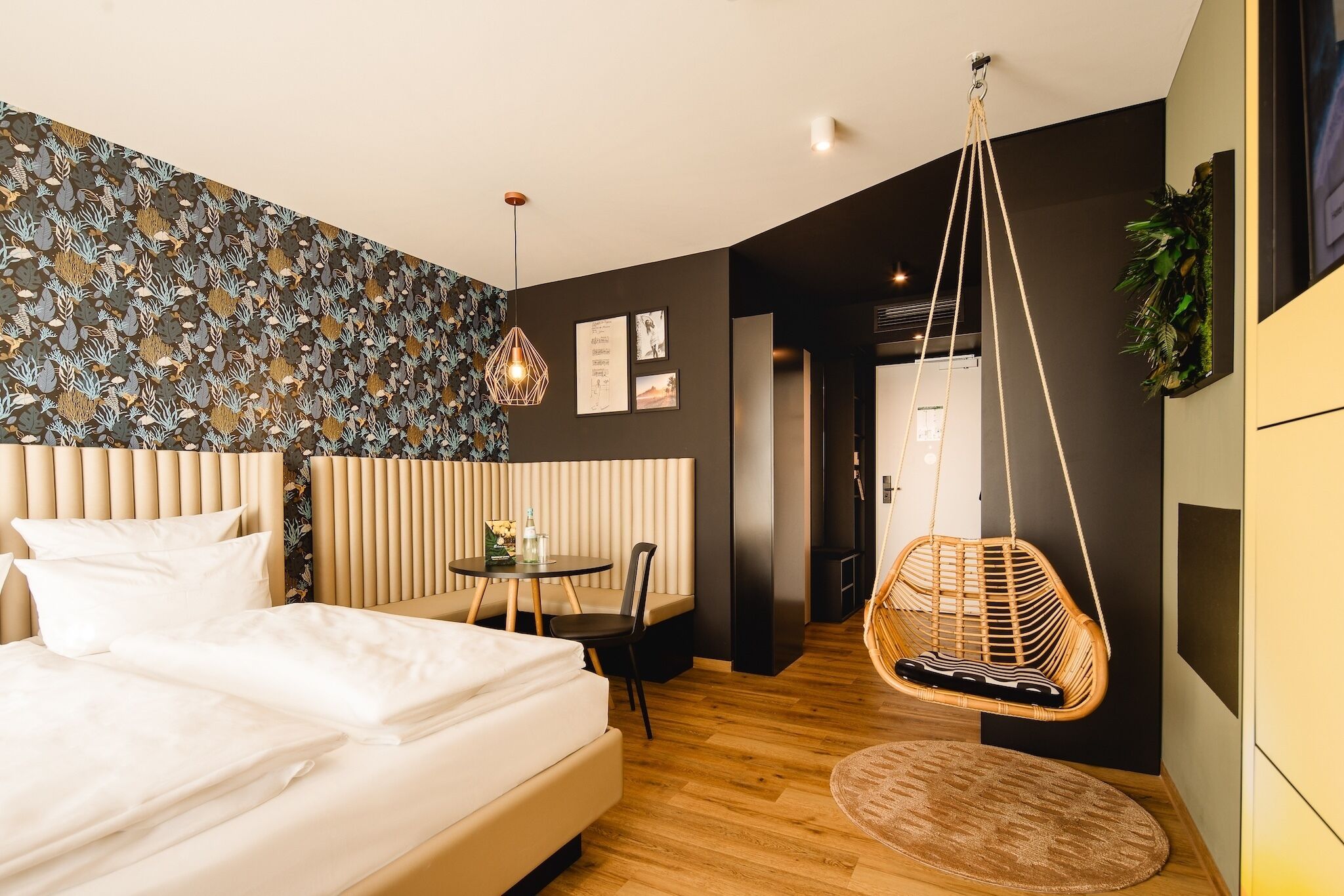 A modern hotel room with a large bed, a small round table, a hanging chair, and a patterned wall.