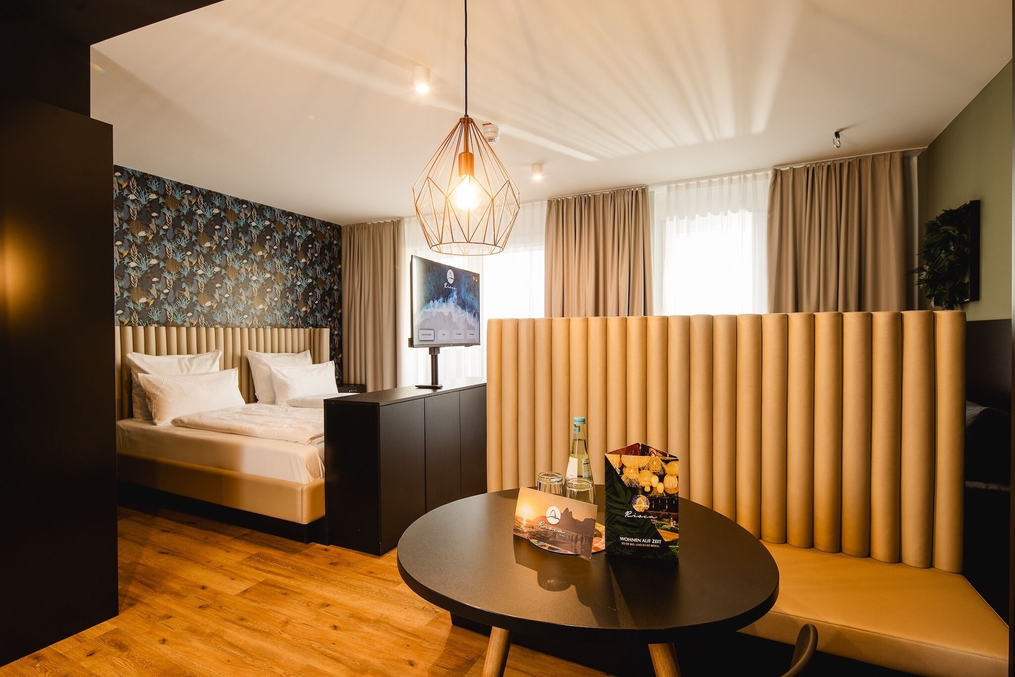 Een moderne hotelkamer met een bed, een ronde tafel met een fles en glazen, en een decoratieve wand.